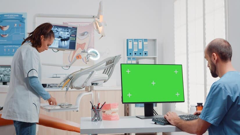 homem usando monitor com tela verde horizontal e conversando com dentista sobre higiene bucal no gabinete especialista