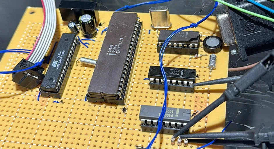 Placa de desenvolvimento com componentes eletrônicos, incluindo um microcontrolador Intel 4004, conectores e fios de teste conectados a diferentes partes do circuito.