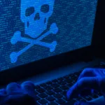 Imagem de um hacker digitando em um laptop com uma caveira representando uma ameaça cibernética exibida na tela, simbolizando uma falha de segurança e ataque cibernético.