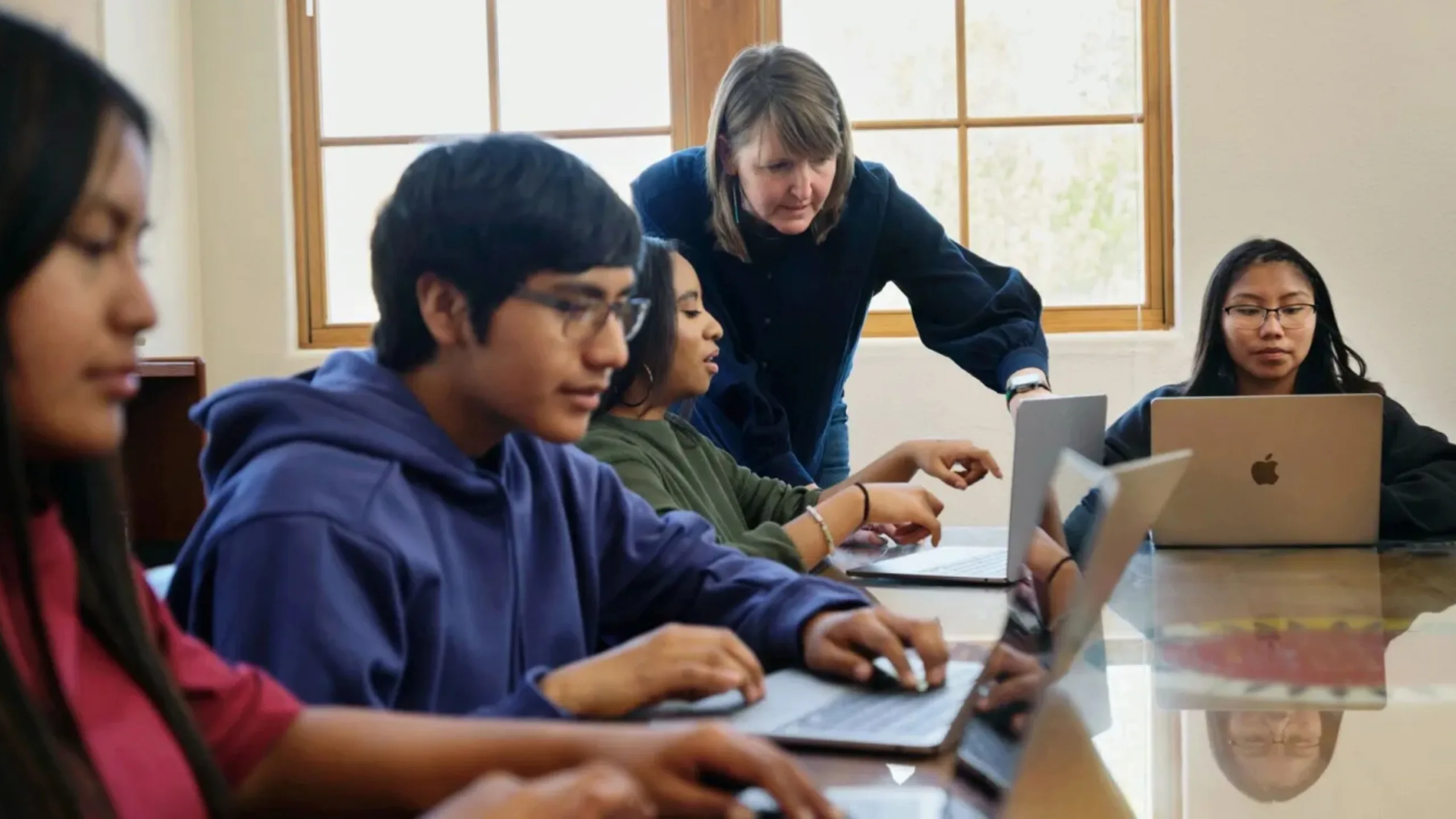 Apple expande os esforços educacionais 2 Imagem com pessoas em volta de motebooks Apple
