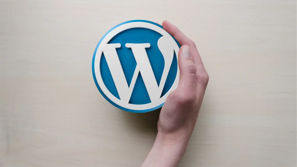 Mão segurando o logotipo do WordPress em fundo de madeira clara