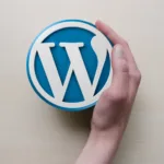 Mão segurando o logotipo do WordPress em fundo de madeira clara