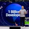 Thomas apresenta na GitHub Universe 2024, com o texto "1 Billion Developers" e um mapa-múndi ao fundo, discutindo a meta do GitHub de conectar desenvolvedores em todo o mundo.