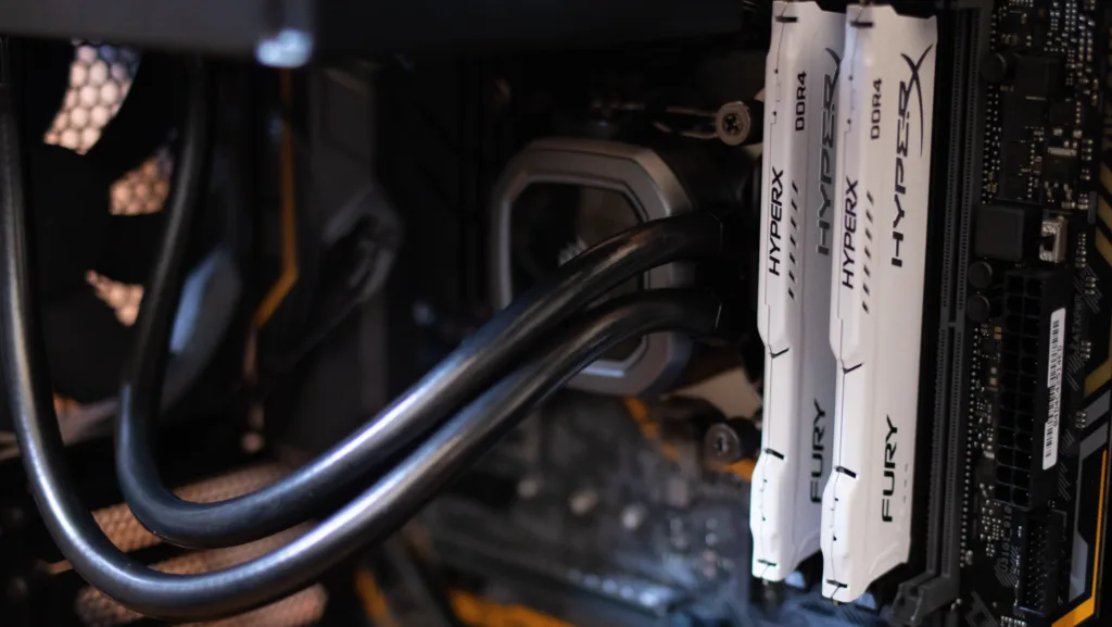 Close-up de módulos de memória RAM DDR4 HyperX instalados em um computador, com detalhes do sistema de refrigeração líquida e componentes internos, representando tecnologia de hardware de alto desempenho.