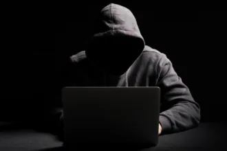 Cibercriminoso operando laptop em ambiente escuro representando agentes de IA em cibersegurança