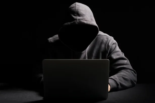 Cibercriminoso operando laptop em ambiente escuro representando agentes de IA em cibersegurança