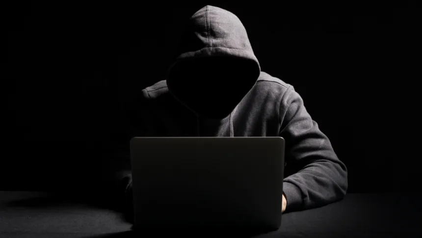 Cibercriminoso operando laptop em ambiente escuro representando agentes de IA em cibersegurança