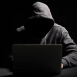 Cibercriminoso operando laptop em ambiente escuro representando agentes de IA em cibersegurança