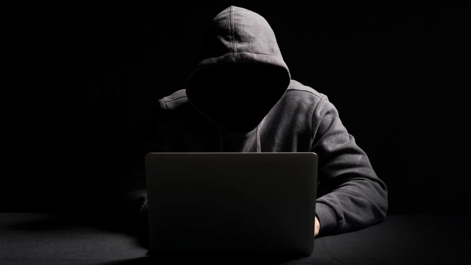 Cibercriminoso operando laptop em ambiente escuro representando agentes de IA em cibersegurança
