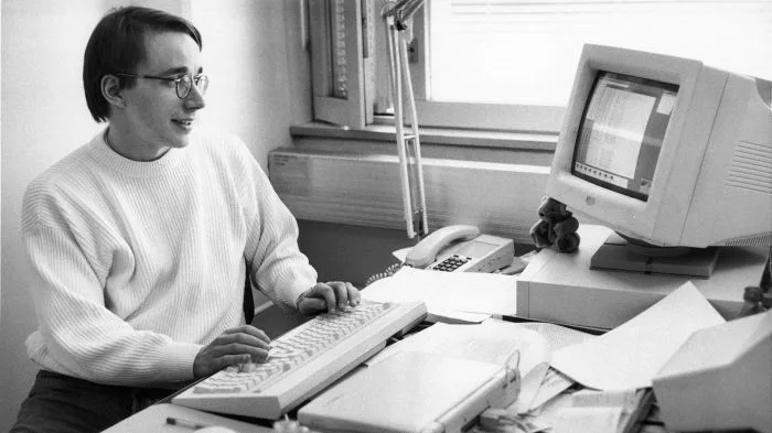Linus Torvalds sentado diante de um notebook, com um terminal do Linux aberto, cercado por ícones de software livre e o logotipo do Git, em estilo minimalista e técnico.