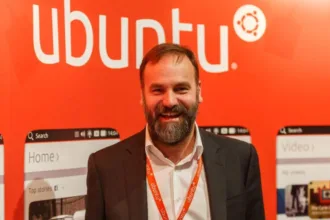 Mark Shuttleworth, pai do Ubuntu, sorrindo diante de painel com o logotipo da distribuição Linux.