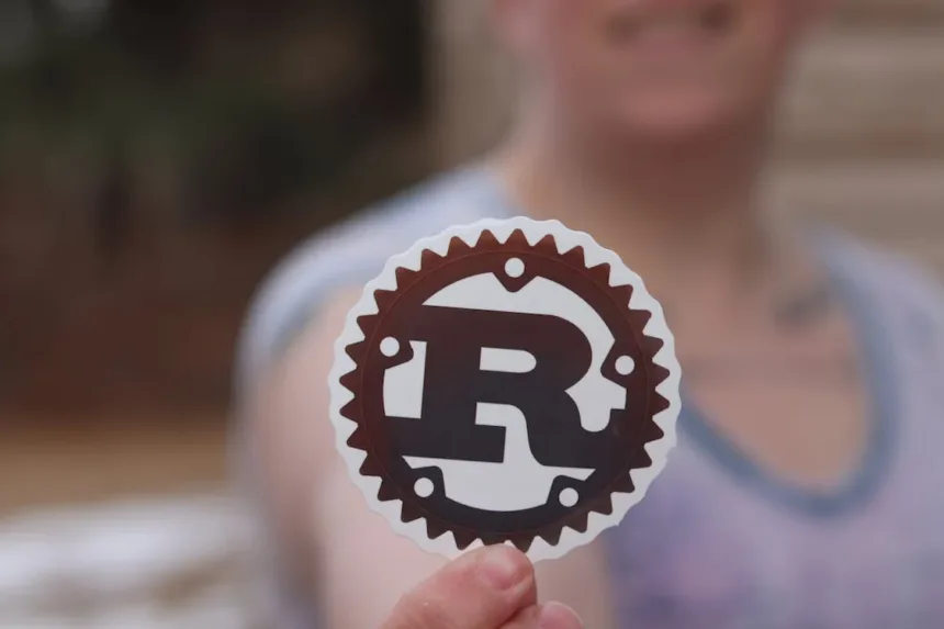 Pessoa segurando adesivo com o logotipo oficial da linguagem Rust, simbolizando o envolvimento com a programação em Rust no Linux.