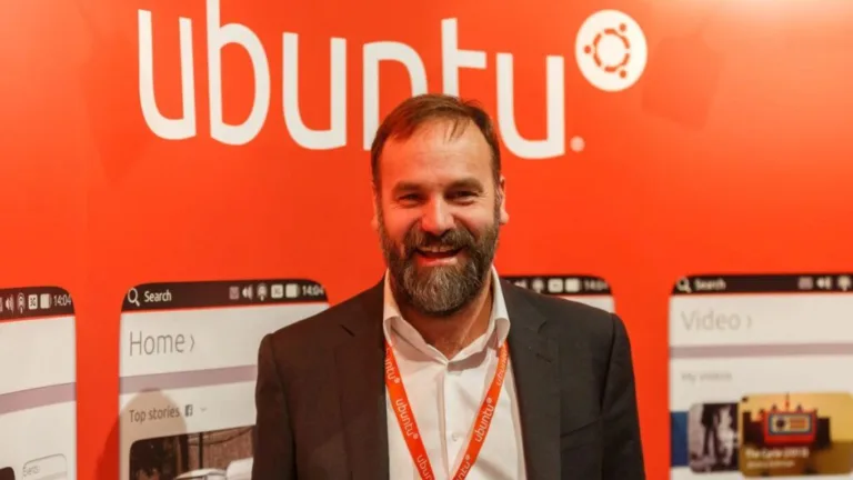 Mark Shuttleworth, pai do Ubuntu, sorrindo diante de painel com o logotipo da distribuição Linux.
