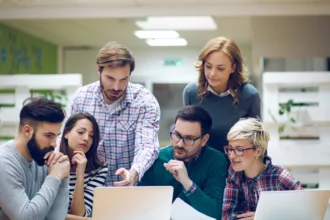 Gestor de TI orienta equipe de desenvolvedores durante code review, ilustrando colaboração e soft skills no ambiente corporativo.