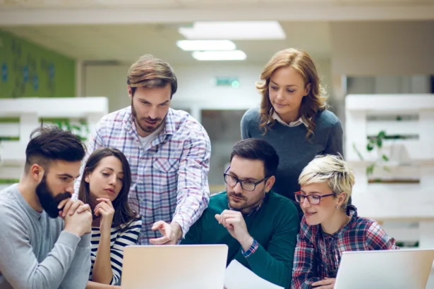 Gestor de TI orienta equipe de desenvolvedores durante code review, ilustrando colaboração e soft skills no ambiente corporativo.