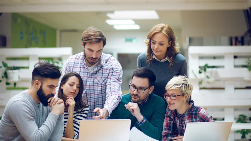 Gestor de TI orienta equipe de desenvolvedores durante code review, ilustrando colaboração e soft skills no ambiente corporativo.