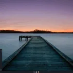 Área de trabalho padrão do Liya Linux 2.4 “Shravya” com papel de parede de pôr do sol, painel inferior e menu de aplicativos aberto