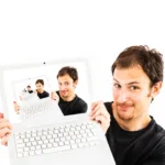 Homem segurando laptop branco com a tela mostrando recursivamente a mesma imagem, representando a janela infinita no terminal Linux com múltiplas instâncias em sequência