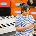 Pessoa segurando smartphone e comparando suporte de software, assistência técnica e valor de revenda do aparelho