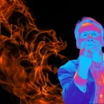 Homem de óculos em efeito térmico, de terno, faz gesto do dedo do meio diante de chamas em fundo preto